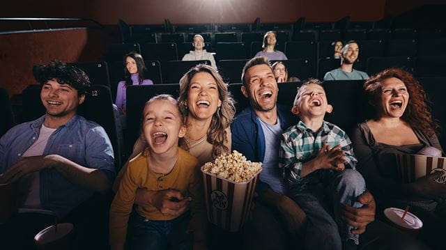 Cheerful family having fun while watching a funny movie in full cinema.